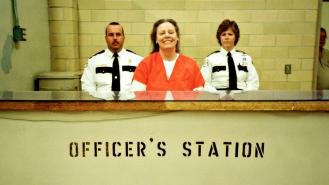 Aileen Wuornos smiling in an orange prison jumpsuit at the officer's station