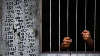 A prisoner behind bars with dates written on the prison walls