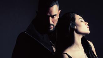 A man looks menacingly over a woman's shoulder at the camer