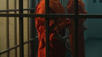 Two prisoners in orange jumpsuits with their hands behind their backs