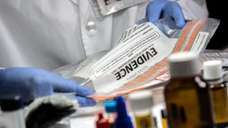 An investigator handles an evidence bag while wearing blue gloves