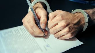 A man signing a document while wearing handcuffs