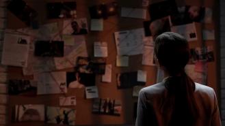A female detective looking at a criminal investigation evidence board
