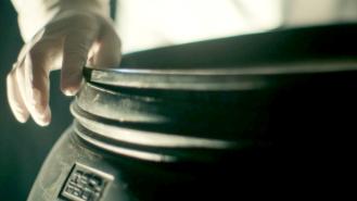 A person with a latex glove on sealing the lid of a large plastic barrel