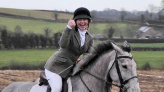 Katie Simpson gives a thumbs up while riding a horse