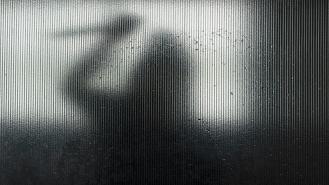 Silhouette of someone wielding a knife behind frosted glass