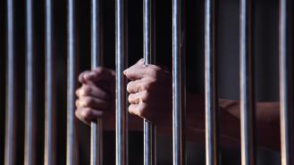 A man holding onto the bars of a prison