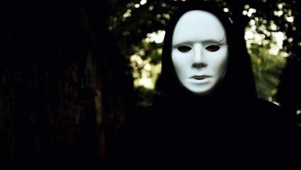 A hooded figure wearing a white mask