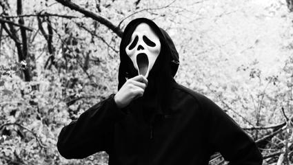 Black and white photo of someone wearing the Scream ghost faced killer costume