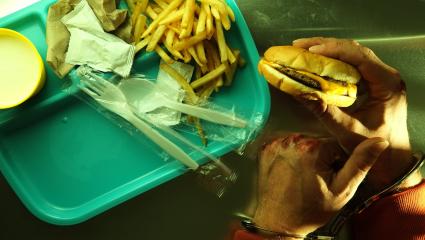 A handcuffed man with bloody knuckles holds a cheeseburger and french fries