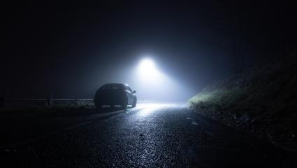 A lone car parked on the side of a rural road on a dark winter's night