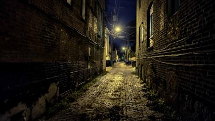 Dark and eerie urban city cobblestone brick paved alley at night