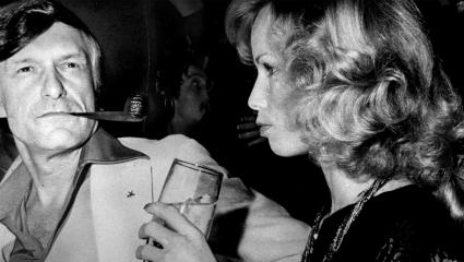 Hugh Hefner smoking his pipe next to a model