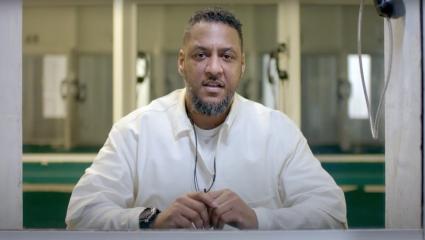 Kenneth Foster sitting behind a screen in a white prisoner uniform