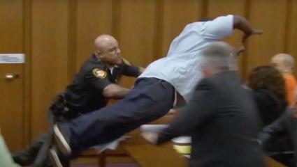 A man jumps over a table in court while a policeman tries to stop him
