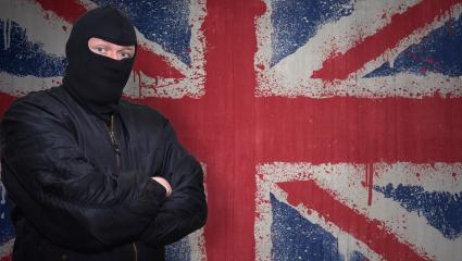 A man in a balaclava stands in front of a British flag