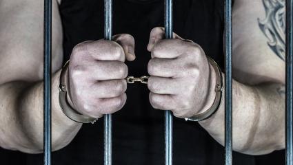 A criminal stands handcuffed in prison