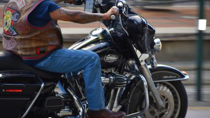 A man in jeans and a biker vest rides a Harley Davidson bike