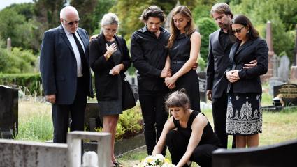 Seven family members dressed in black look solemn as they lay a wreath of flowers on a grave