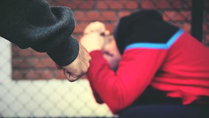 A man cowers while another man approaches with a clenched fist