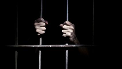 A stock image of a person holding onto jail bars