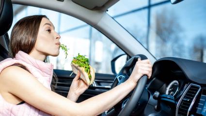 A woman eats a large sandwich while driving a car