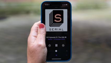 A person holding a mobile phone with the Serial podcast logo displayed on the screen