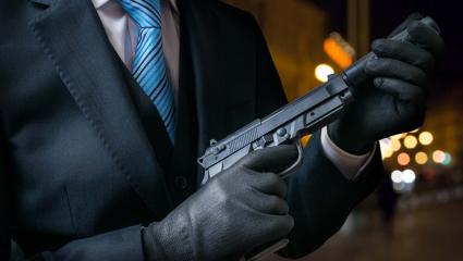 A man in a suit holds a pistol with a silencer