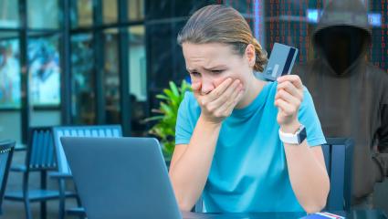A woman holding a credit card holds her mouth in shock while browsing the internet