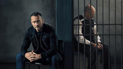 Will Mellor next to a policeman in a prison cell