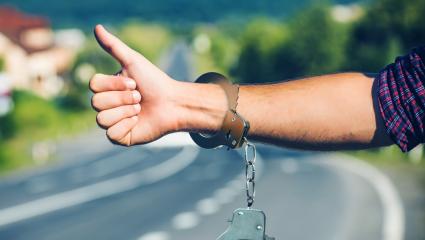 A hitchhiker hailing a lift wearing handcuffs