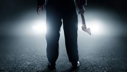A man holds an axe in front of car headlights
