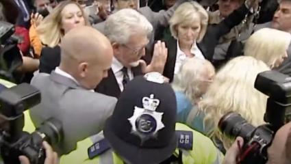 Rolf Harris walking out of court through a melee of police and journalists