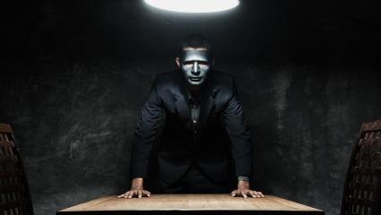 A man with a black mask standing over a desk
