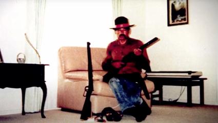Ivan Milat sitting on a couch holding a gun