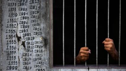 A prisoner behind bars with dates written on the prison walls