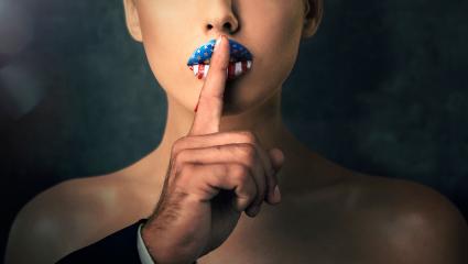 A man pressing his finger against a woman's lips to 'shush' her