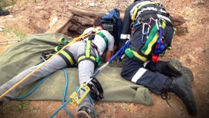 Two rescuers look in a hole in the outback
