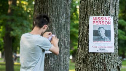 A man pinning 'Missing Person' posters to trees