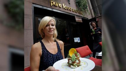Sarma Melngailis holding a plate of food in front of a Pure Food and Wine restaurant in New York