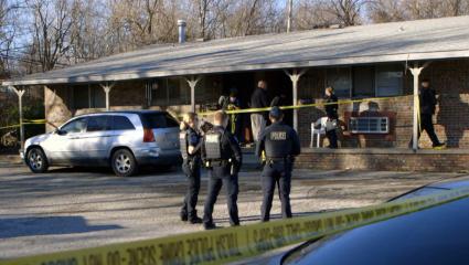 Police officers stand outside a crime scene, while other officers inspect the building