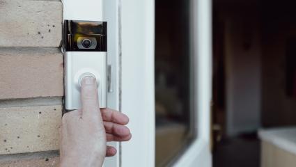 A person pressing a smart doorbell with their thumb