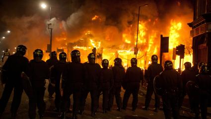 Armed riot police watch a large building on fire in Tottenham