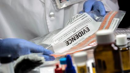 An investigator handles an evidence bag while wearing blue gloves