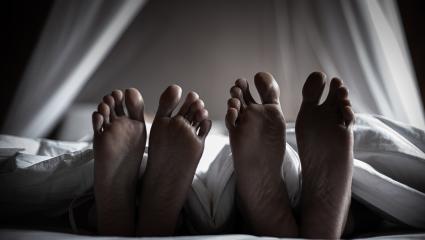 Two pairs of feet stick out the bottom of a duvet