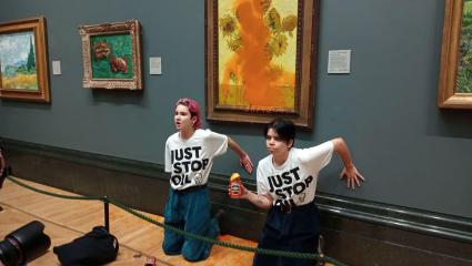 Phoebe Plummer and Anna Holland with their hands glued to the wall beneath Van Gogh's 'Sunflowers' which they have thrown tomato soup over