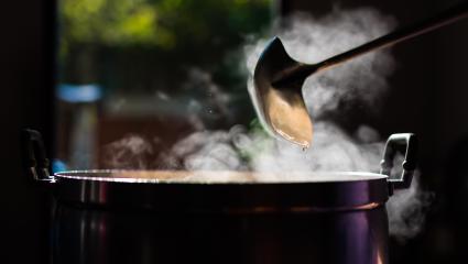 A ladle is used in a large pot which is steaming