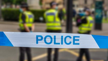 Police tape in front of three British police officers