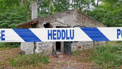 Police tape reading 'Heddlu' in front of an abandoned stone building