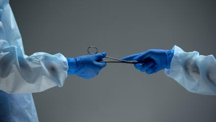 Two people performing a medical operation passing a tool between them